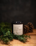 Candle labeled 'Azriel' with greenery and pinecones on a dark background