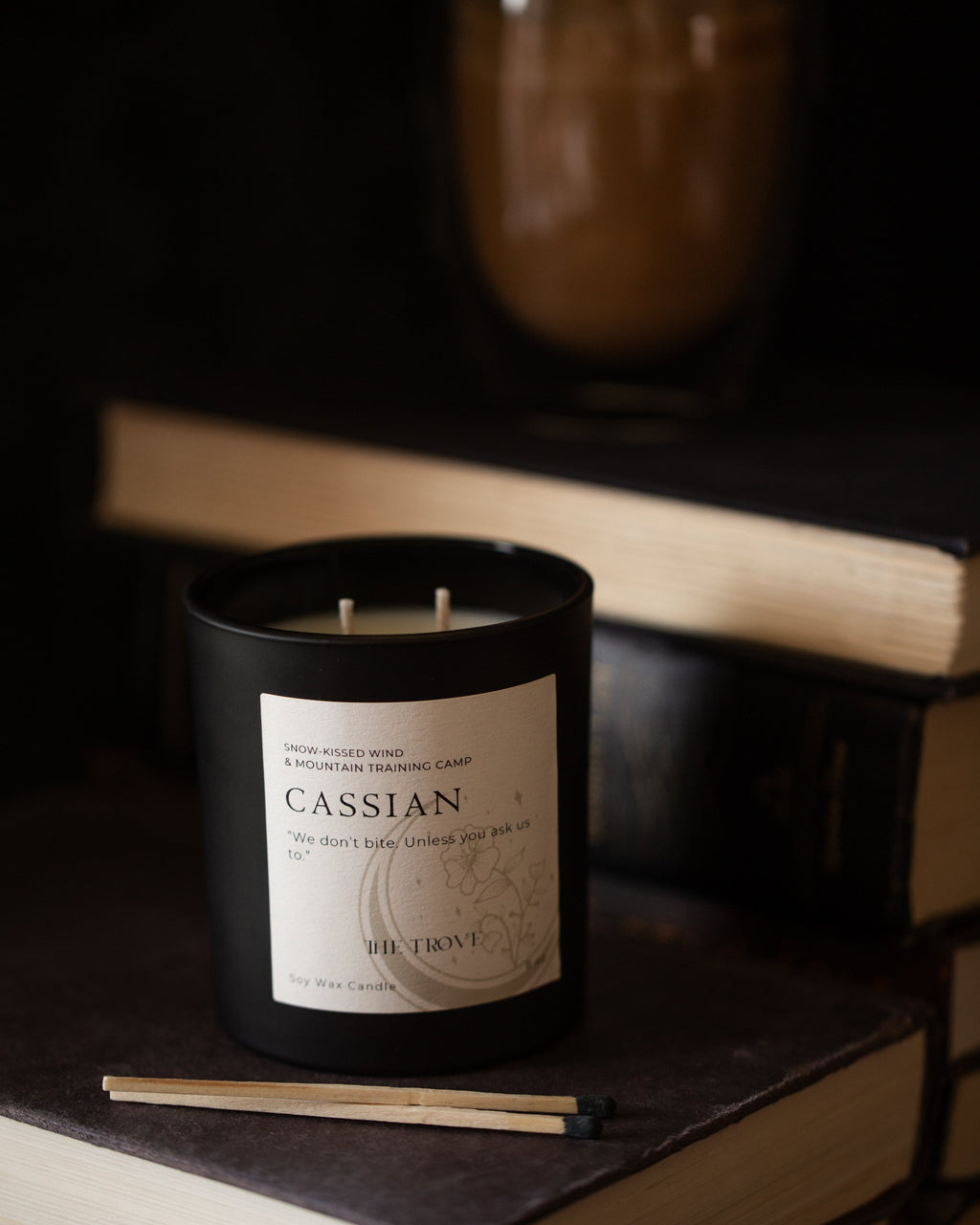 Candle labeled 'Cassian' on a stack of books with a dark background