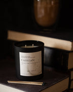 Candle labeled 'Cassian' on a stack of books with a dark background