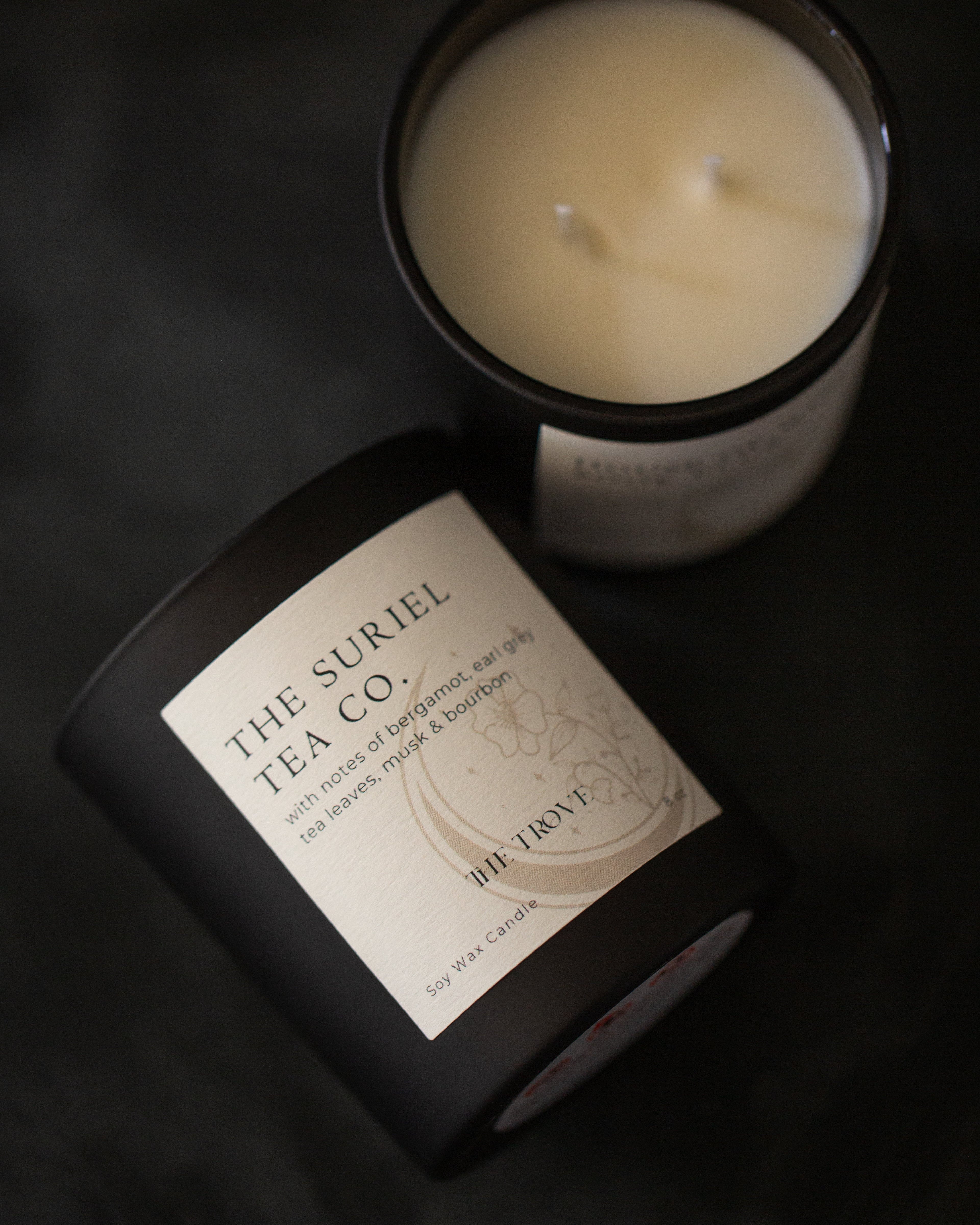 Candle in black jar with the Suriel Tea Co. on the label on a dark background