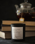 candle in black jar with 'The Suriel Tea Co.' label in front of a teapot and books on a dark background