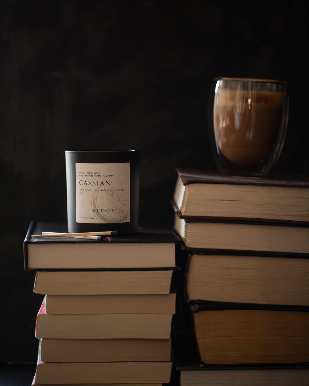 Stack of books with a candle labeled 'Cassian' and a glass of coffee against a dark background