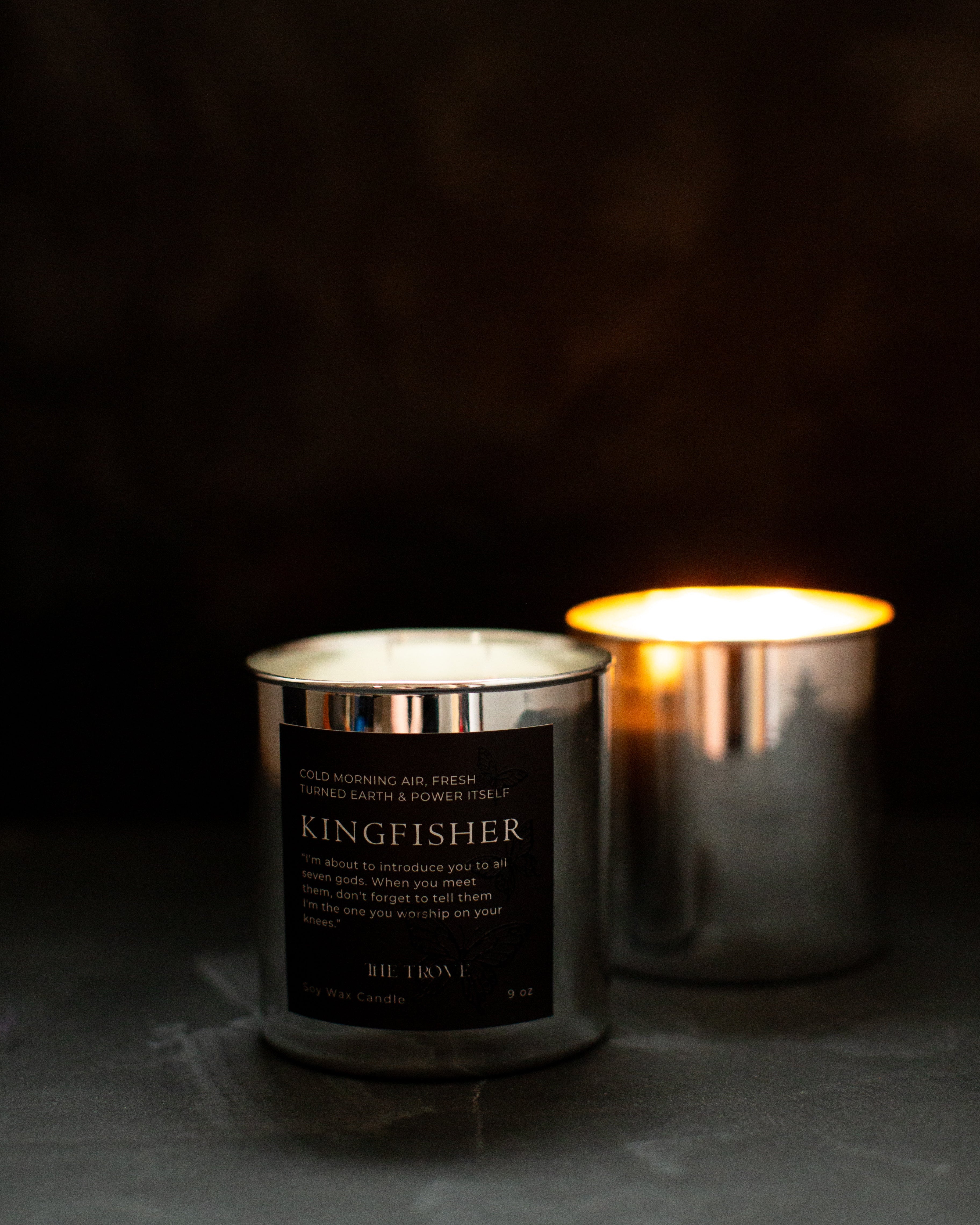 Two candles, one lit and one unlit, on a dark surface with a dark background.