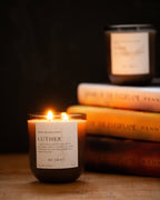 Candle labeled 'Luther' by Tovve on a wooden surface with books in the background.