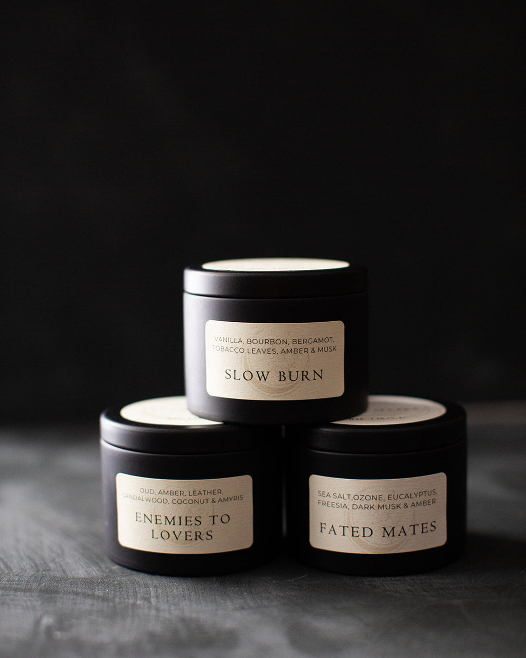 Three black candles stacked on a dark surface with visible labels.