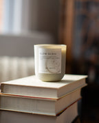 Candle labeled 'Slow Burn' on a stack of books with a blurred background