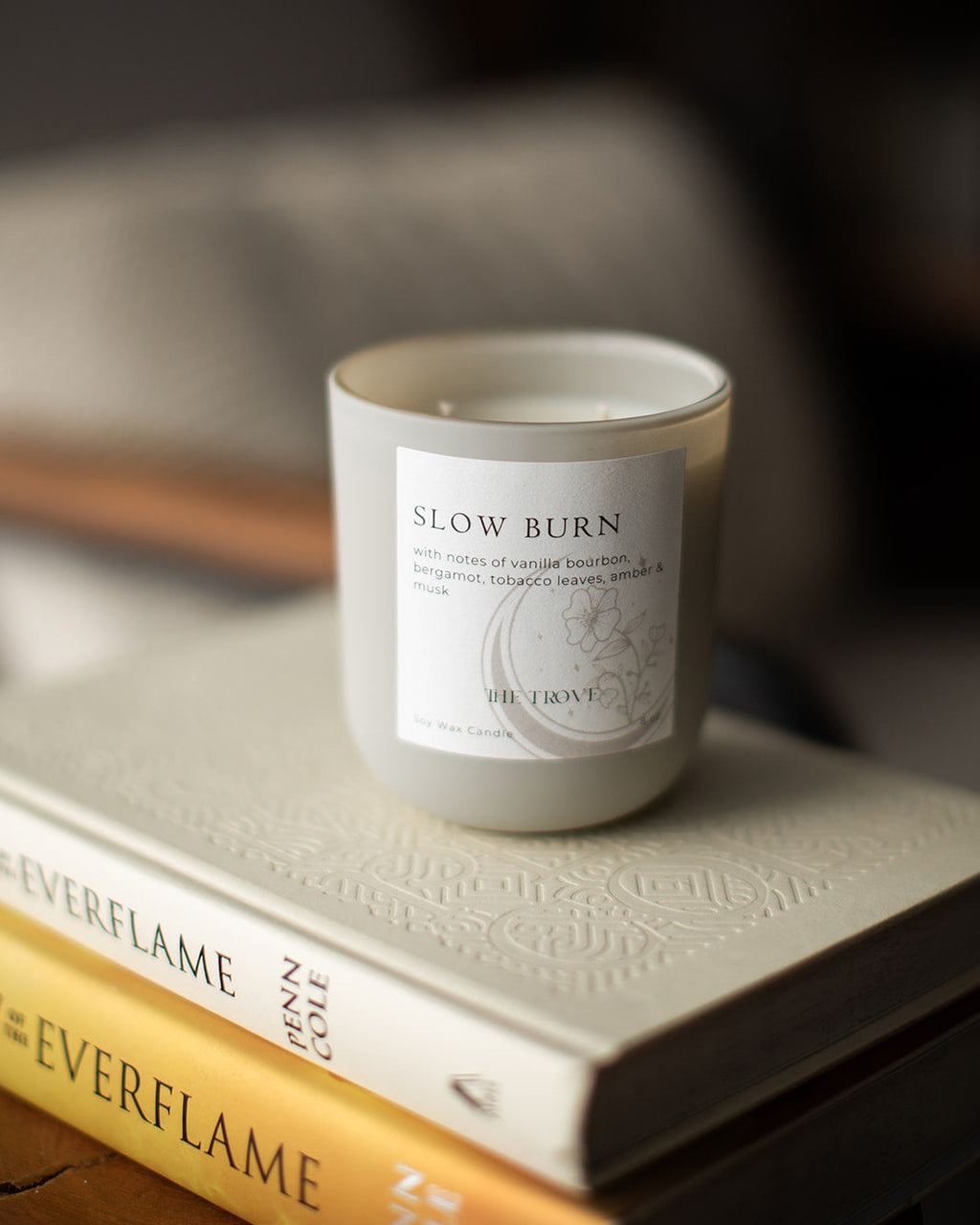 Candle labeled 'Slow Burn' on a stack of books with a blurred background