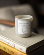 Candle labeled 'Slow Burn' on a stack of books with a blurred background