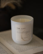 Candle labeled 'TBR List' on an open book with a dark background