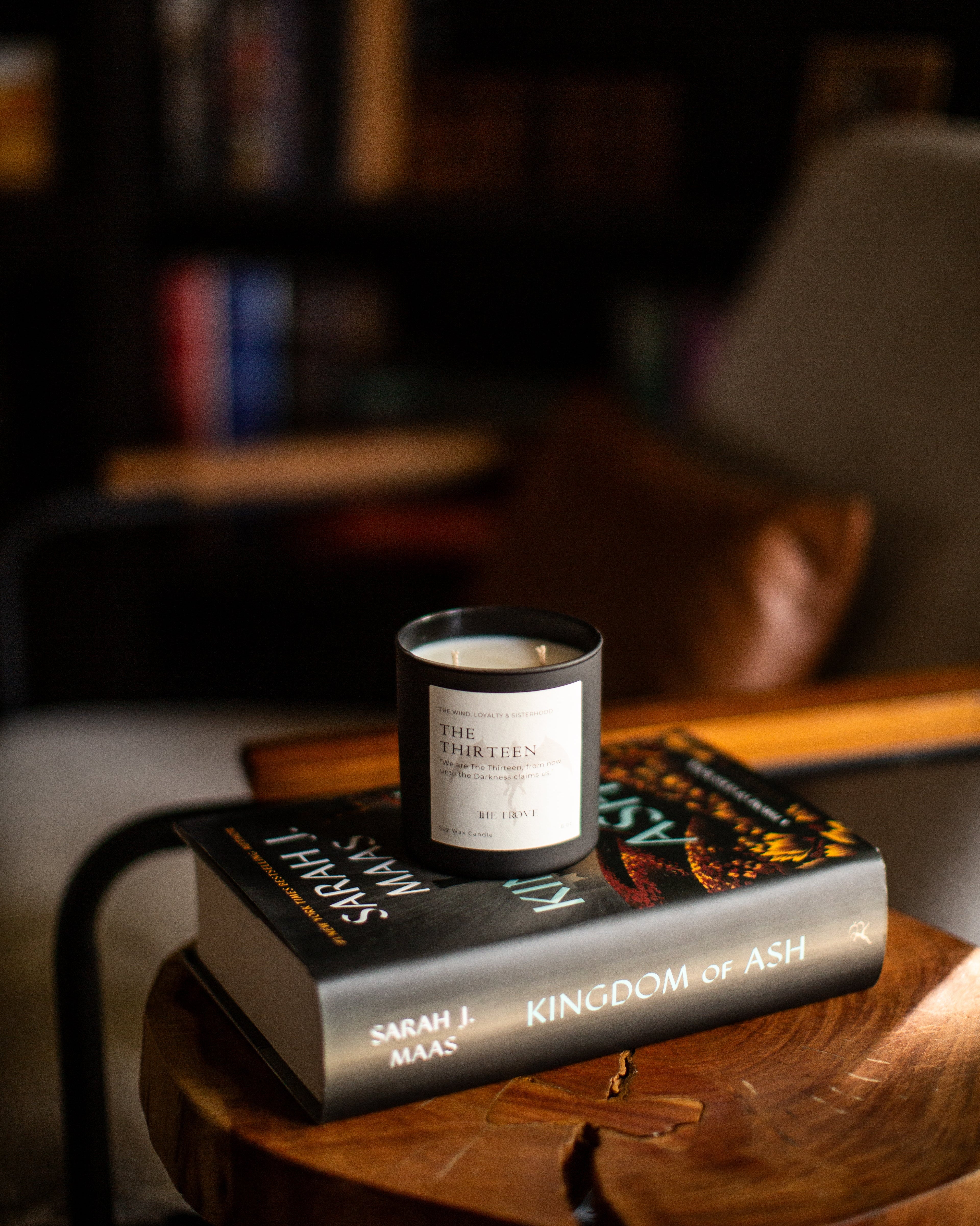 Candle on a book titled 'Kingdom of Ash' by Sarah J. Maas, with a blurred background