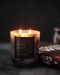 Candle labeled 'Xaden' with a book titled 'Fourth Wing' in the background on a dark surface.