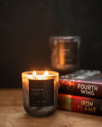 Candle labeled 'Xaden' with books in the background on a wooden surface