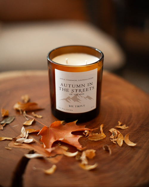 Candle labeled 'Autumn in the Streets' on a wooden surface with fall leaves.