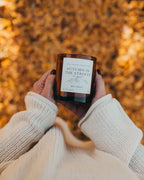 Person holding a candle labeled 'Autumn in the Streets' against a blurred autumn leaf background