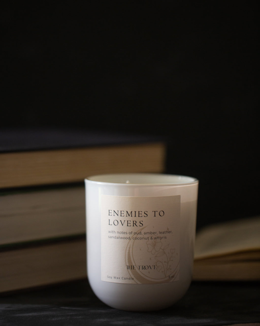Candle labeled 'Enemies to Lovers' with books in the background