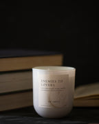 Candle labeled 'Enemies to Lovers' with books in the background