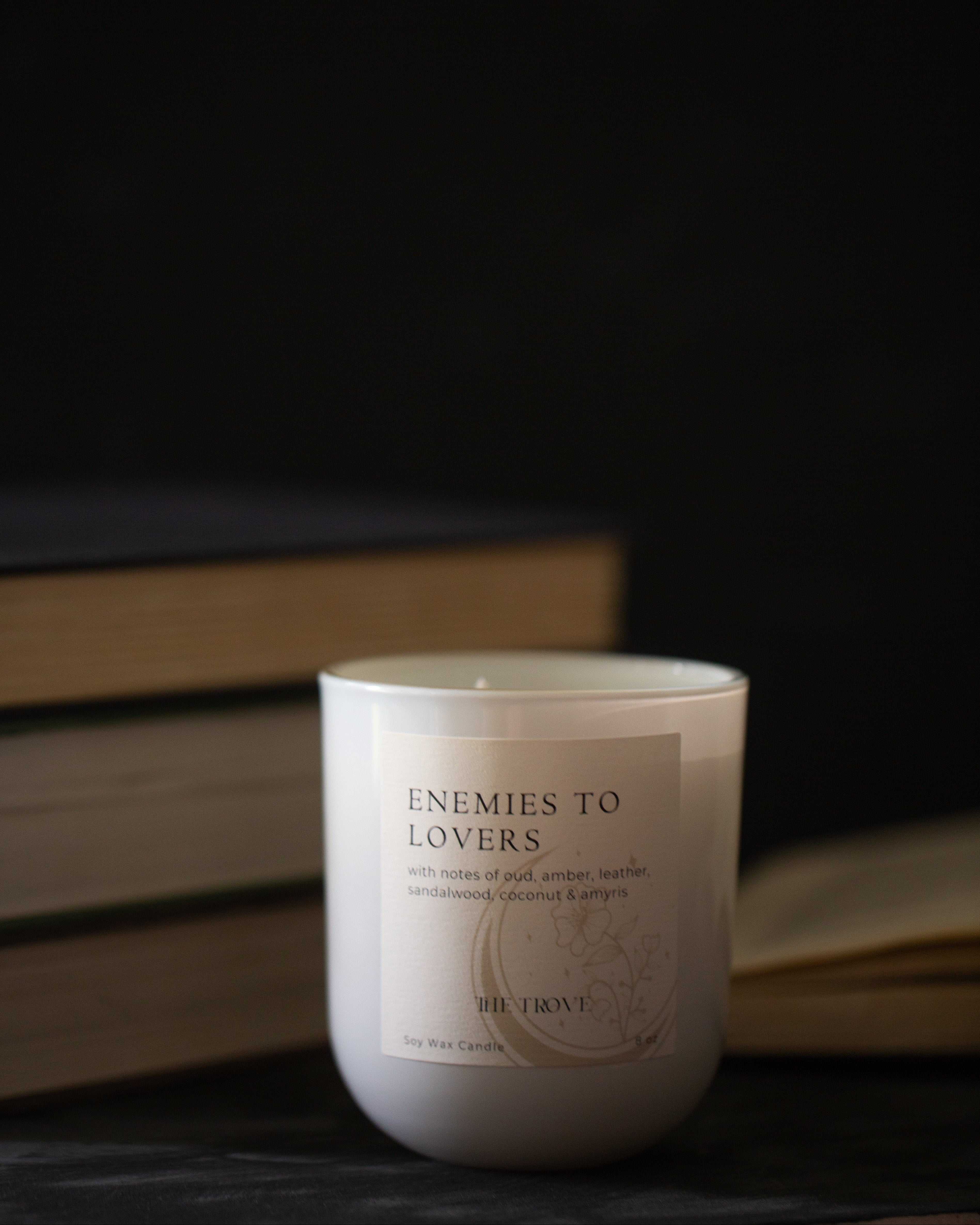 Candle labeled 'Enemies to Lovers' with books in the background