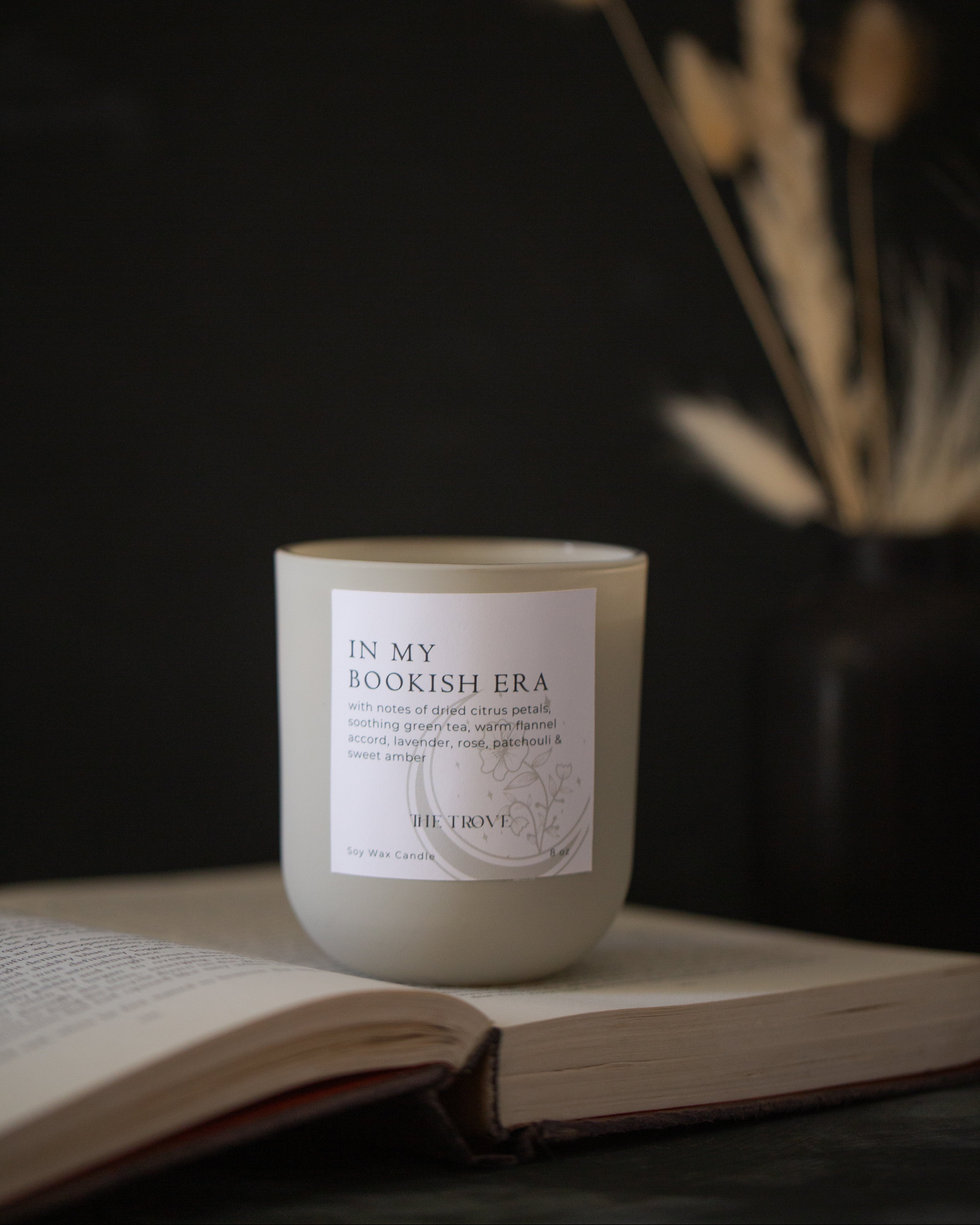 Candle labeled 'In My Bookish Era' on an open book with a dark background