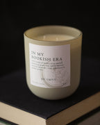 Candle labeled 'In My Bookish Era' on a book with a dark background