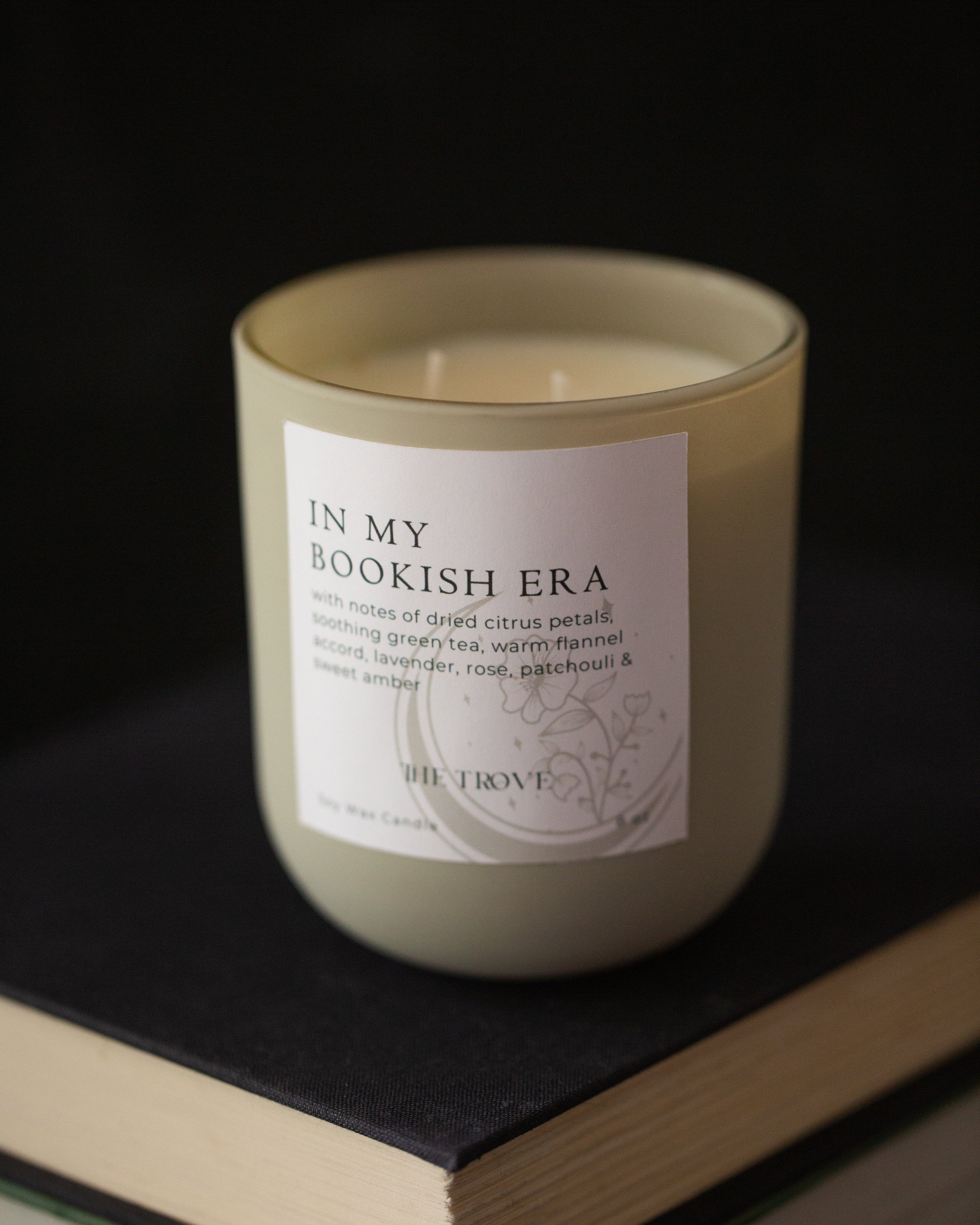 Candle labeled 'In My Bookish Era' on a book with a dark background