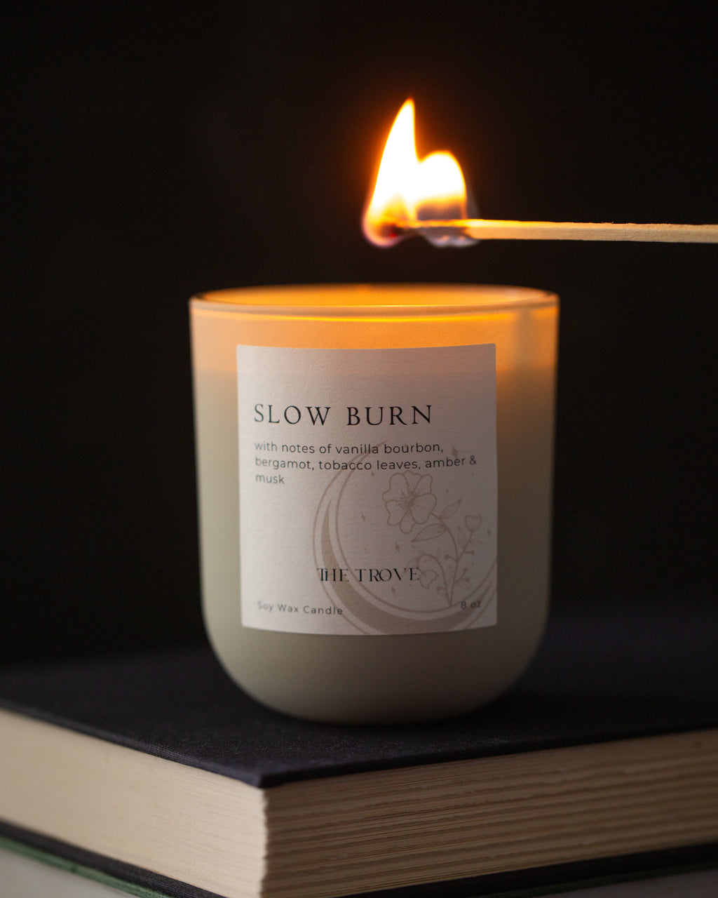 Candle labeled 'Slow Burn' being lit with a match on a dark background