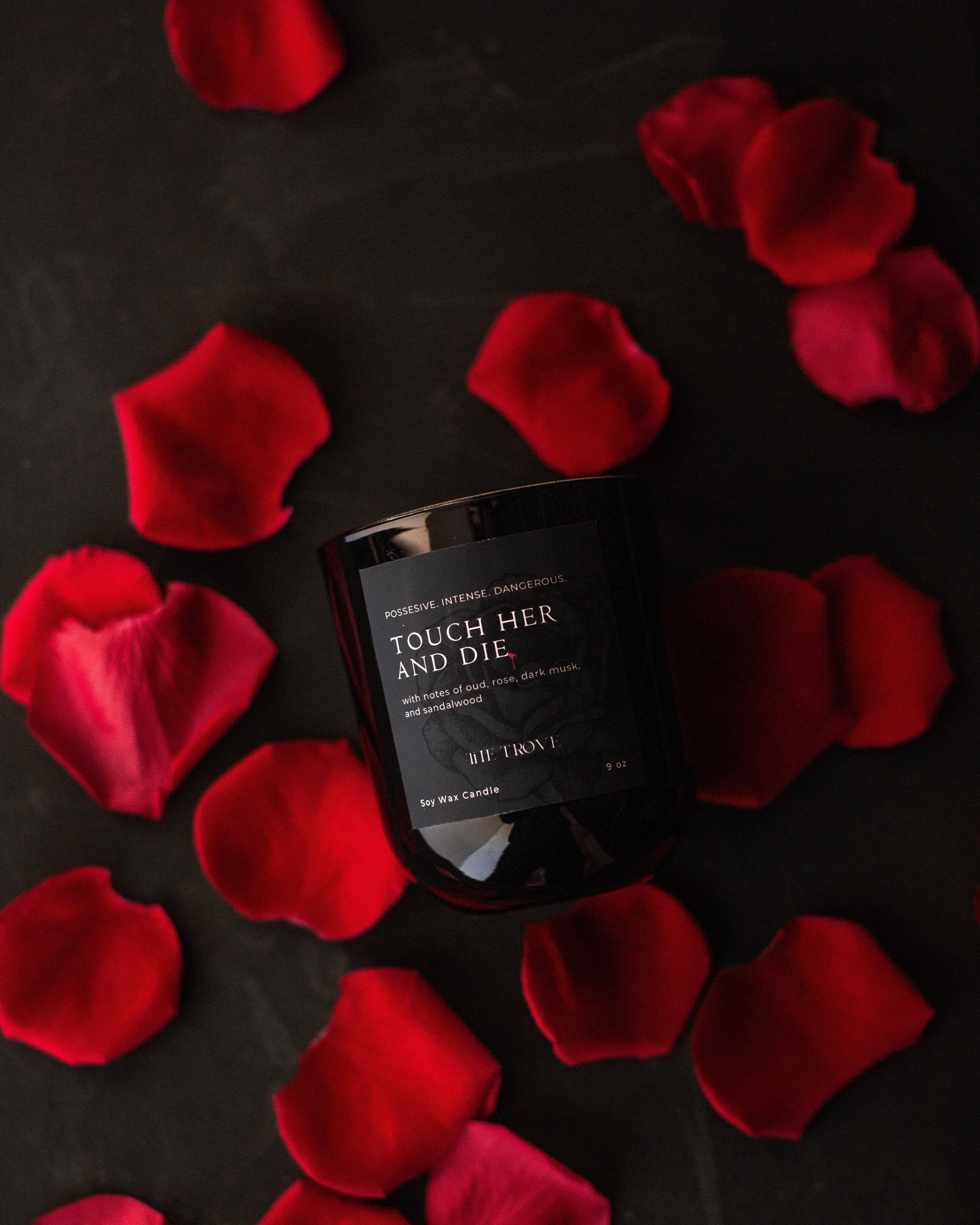 Black bottle labeled 'Touch Her and Die' surrounded by red rose petals on a dark background
