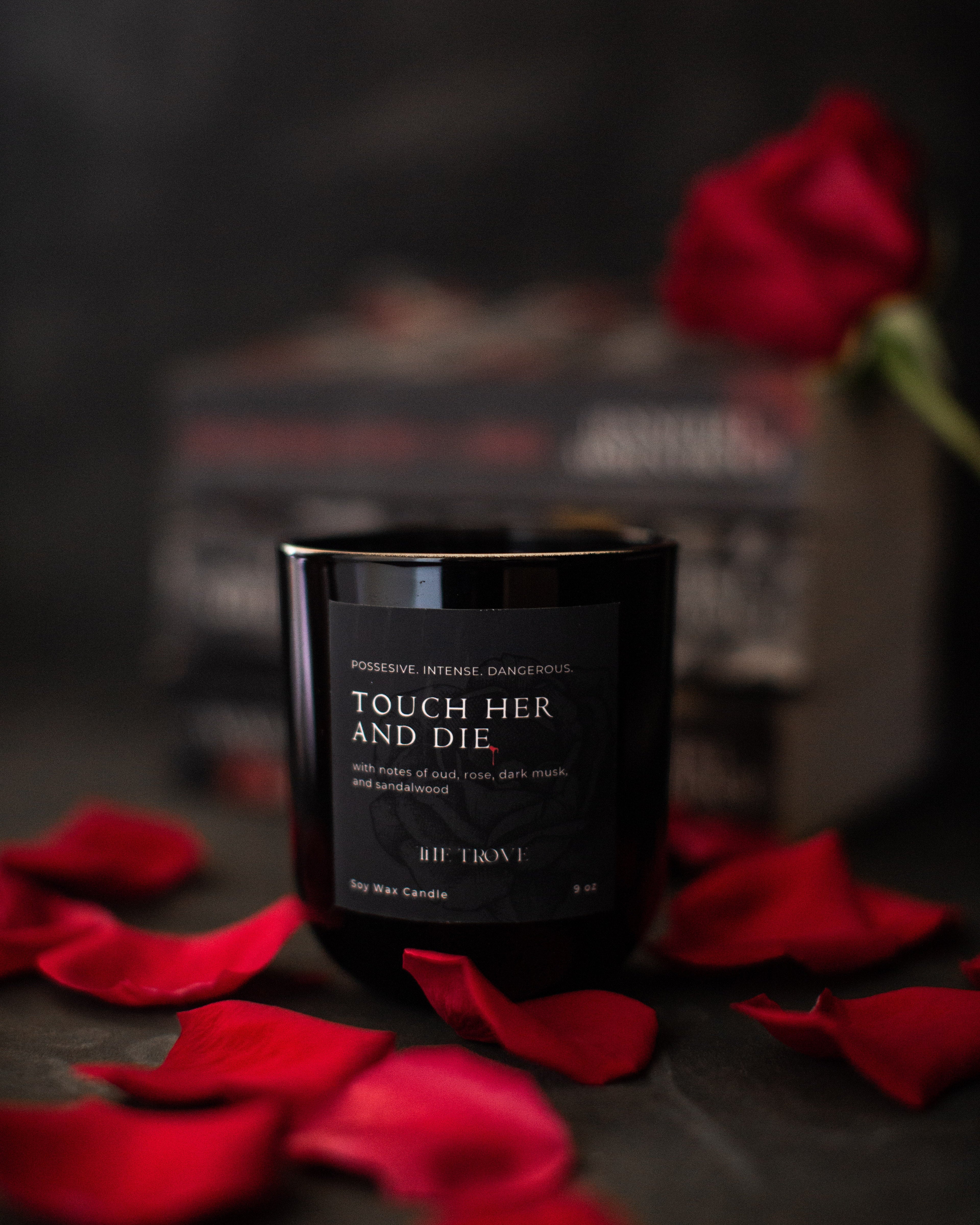 Black candle labeled 'Touch Her and Die' with red rose petals on a dark background