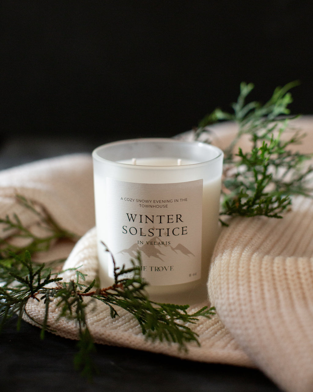 Candle labeled 'Winter Solstice' on a textured surface with greenery