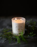 Candle labeled 'Winter Solstice' with greenery on a dark background