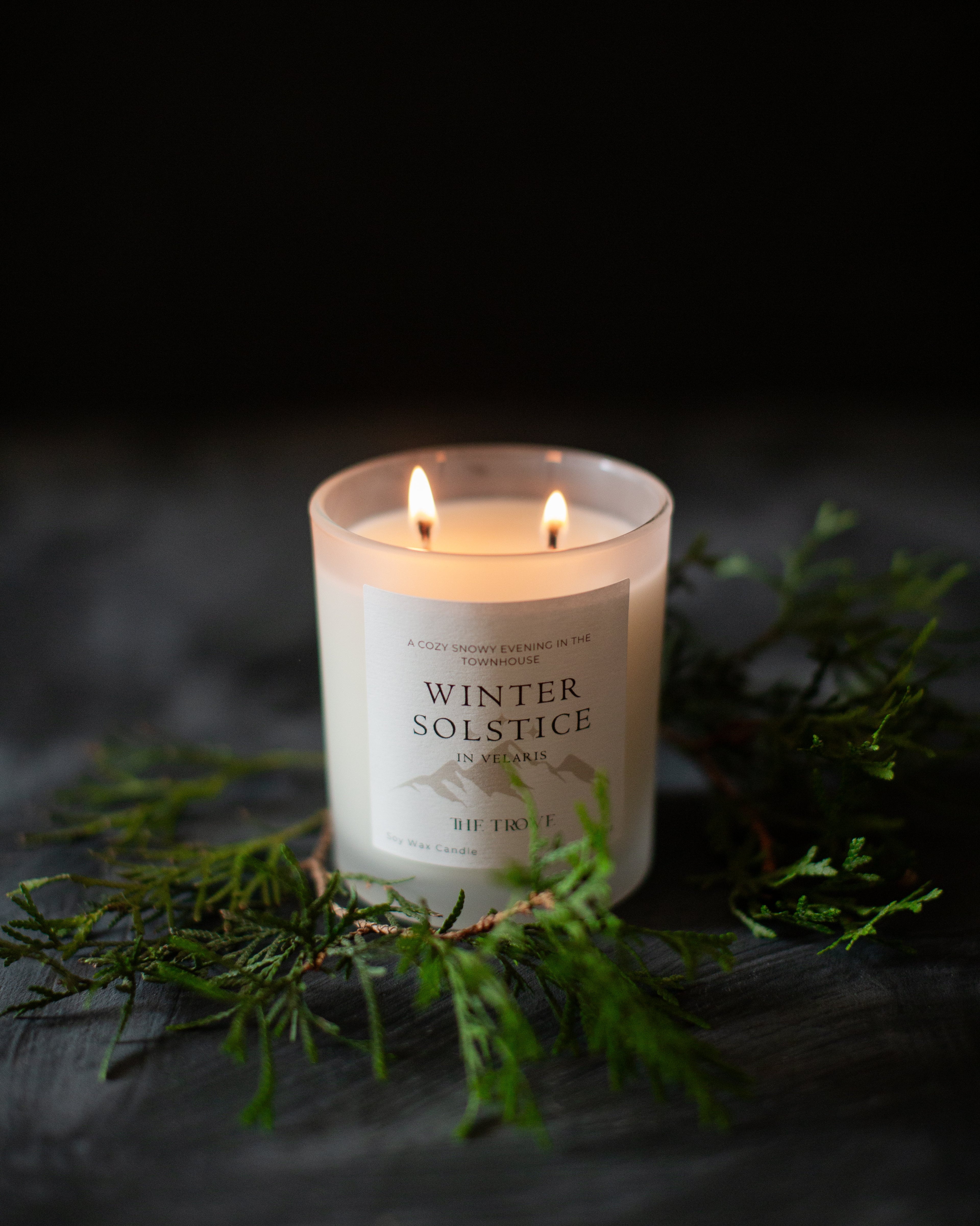 Candle labeled 'Winter Solstice' with greenery on a dark background