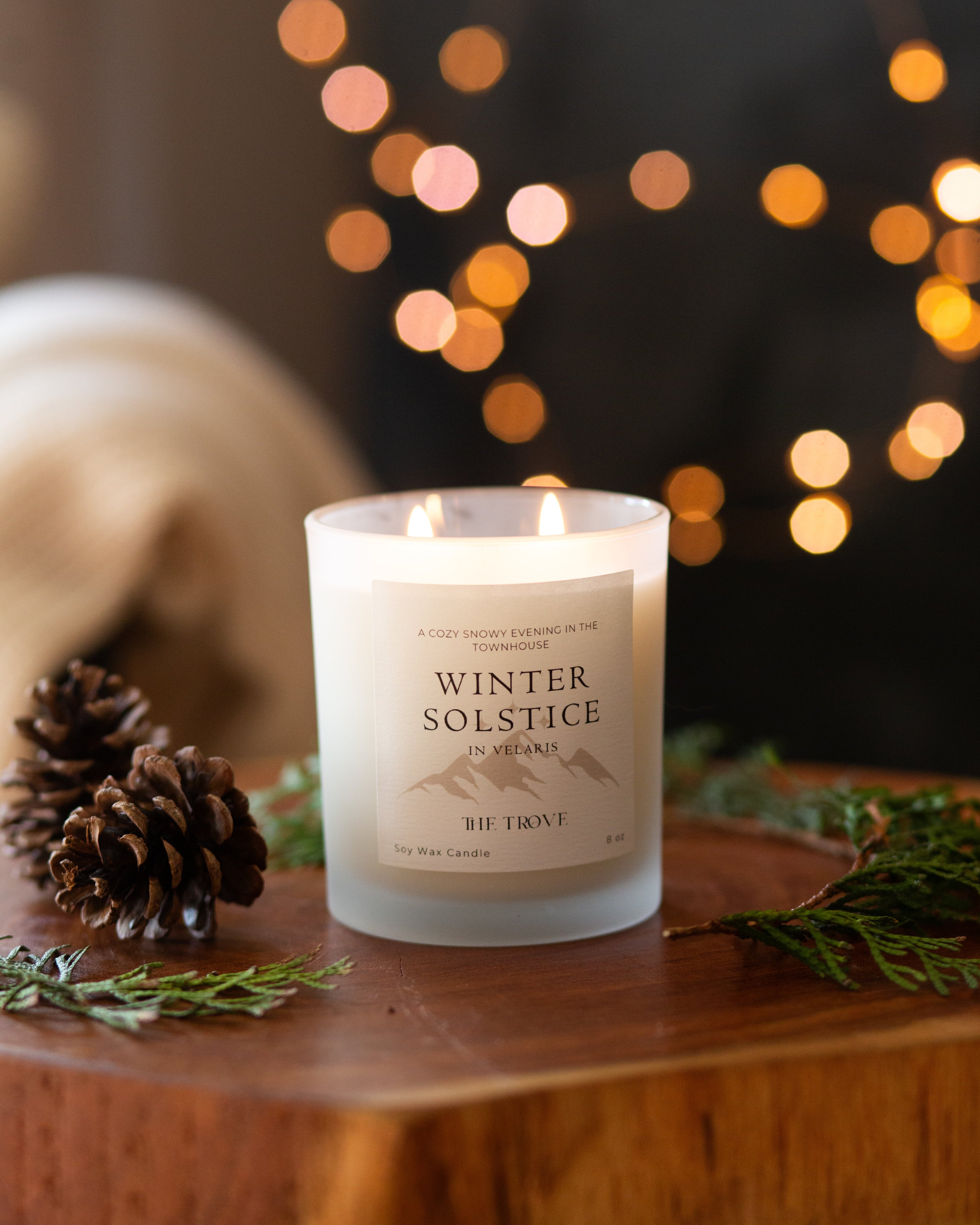 Candle labeled 'Winter Solstice' on a wooden surface with decorative lights in the background